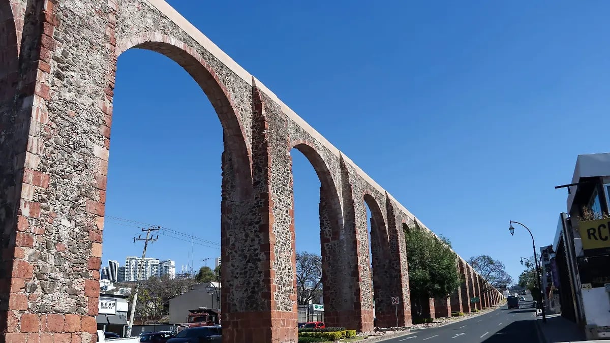 Historic brick aqueduct arches extending into the distance under clear blue sky with city buildings in background