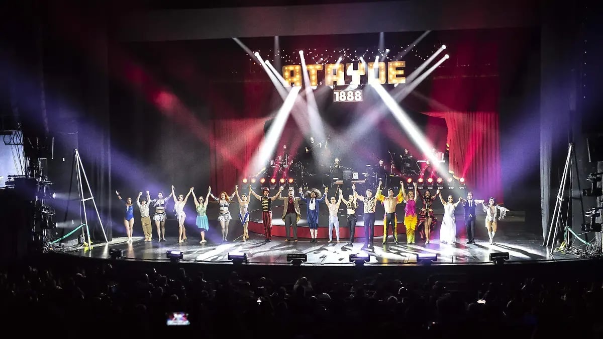Large concert stage with colorful lighting, performers arranged on stage, and audience in foreground at a live music event