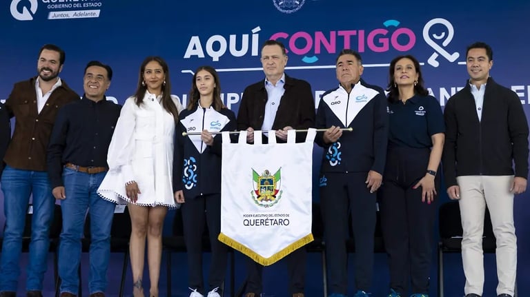 Group of officials and dignitaries standing on stage behind a Querétaro banner at a political rally event