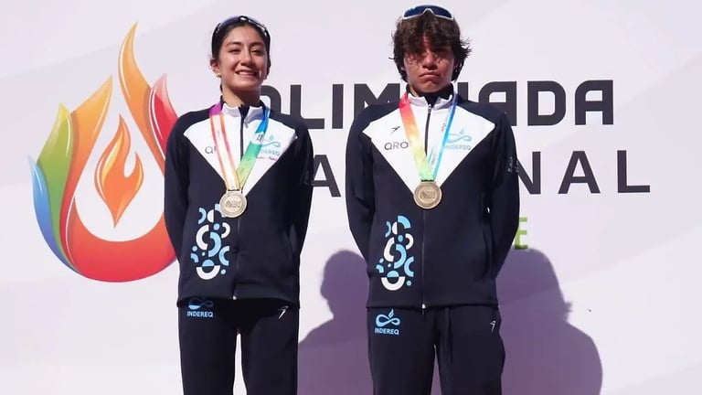 Two male athletes wearing dark blazers and medal ribbons stand in front of an Olympic logo with colorful flame design