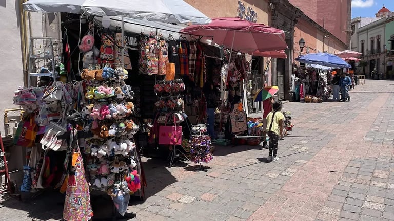 Street vendor stalls with colorful textiles and merchandise under maroon umbrellas in an outdoor market square