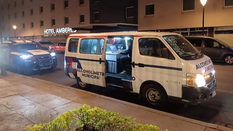 White van marked Alcoholimetres Municipaux parked on a nighttime street with Hotel Ambere building and other vehicles visible